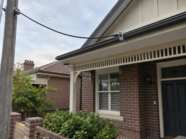 Overhead service cable and bracket on a brick house exterior with eaves and front porch in Chatswood